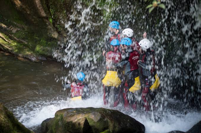 Grupo con neopreno, casco y arnés descendiendo un barranco de aguas cristalinas entre rocas en el Valle de Miera.