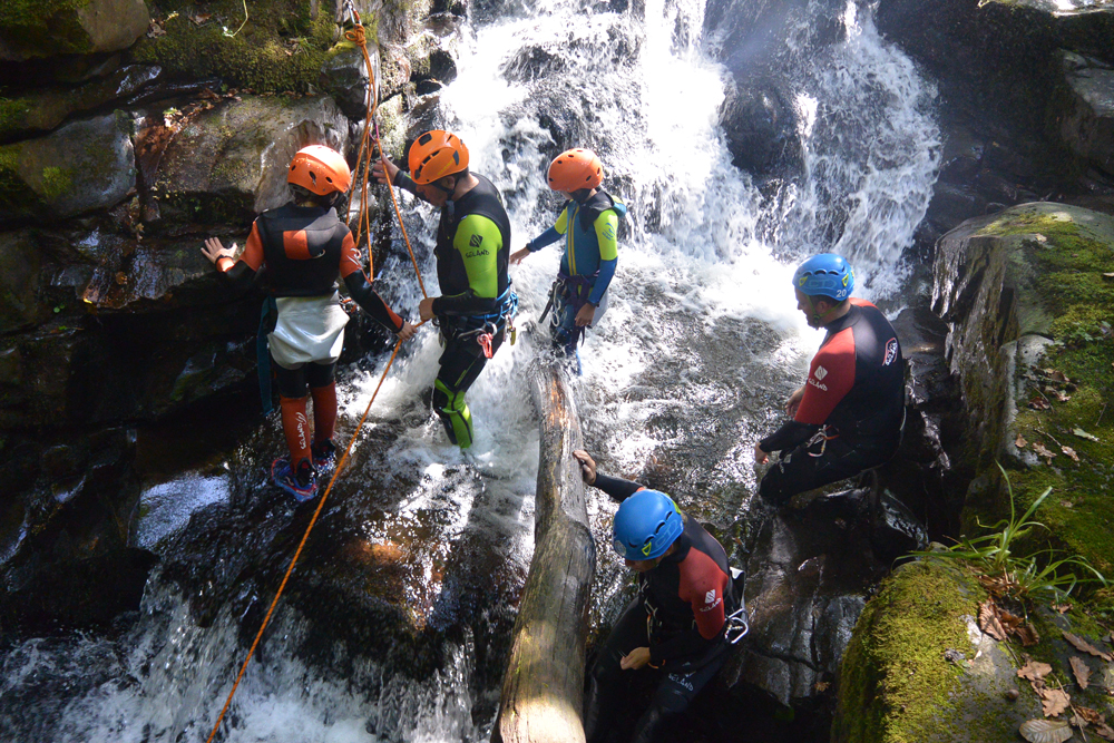 Persona haciendo rápel junto a una cascada dentro de un cañón forestal estrecho, cañón del Aján.