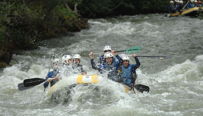 Grupo numeroso repartido en varias balsas de rafting navegando un tramo ancho y tranquilo del río Saja.