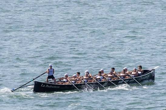 Trainera de remo tradicional compitiendo en la bahía de Santander durante una regata de la Liga ARC1, varias embarcaciones en línea, día soleado.