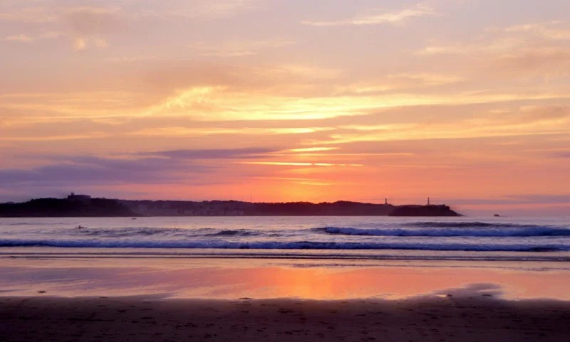 Atardecer en la playa de Loredo con la marea subiendo y siluetas de paseantes