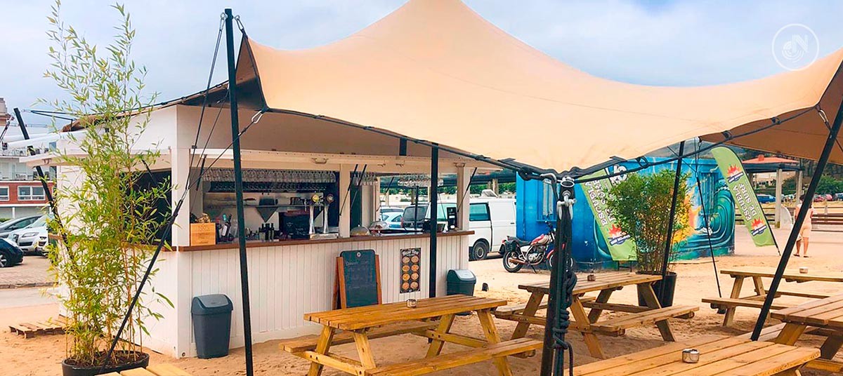 Terraza de madera del Chiringuito La Lagartija en la playa de Cuberris, Ajo, con mesas al aire libre y vistas al mar en un mediodía de verano