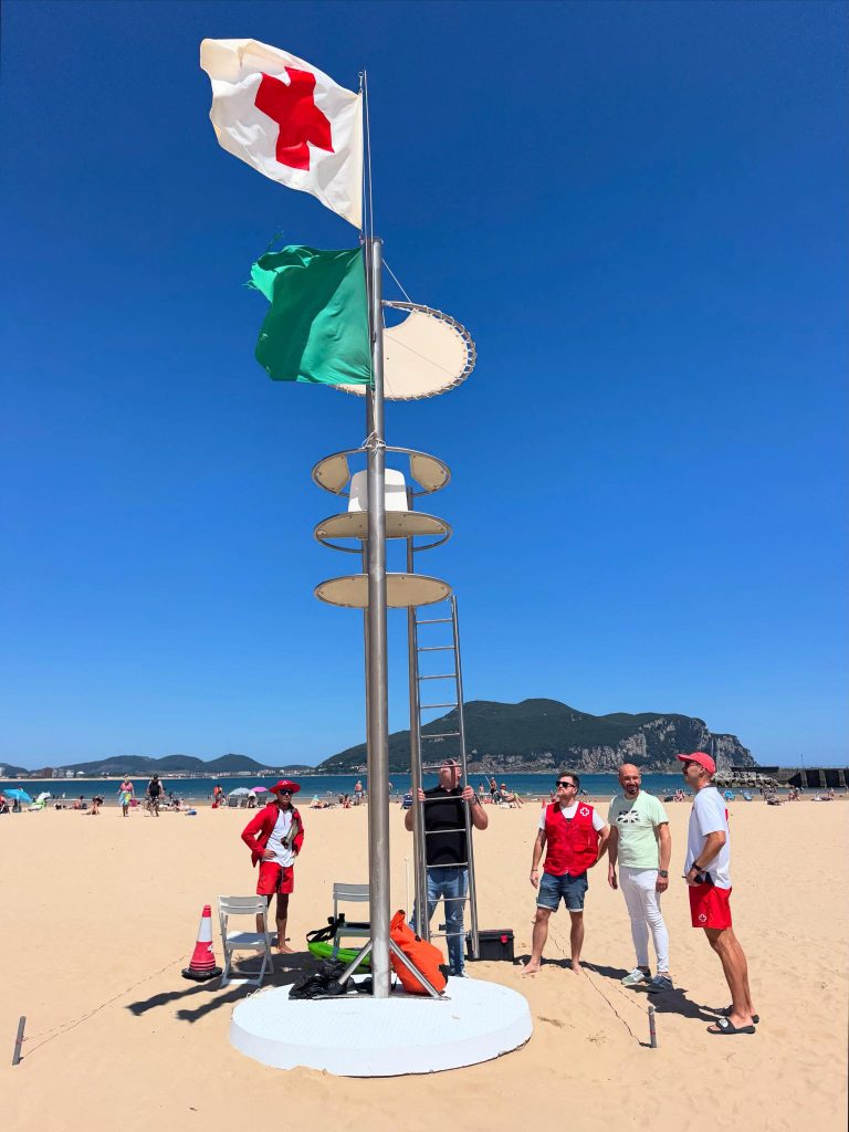 Torre de vigilancia de socorrista izada con bandera verde en una playa de la costa oriental de Cantabria (zona de Noja o Laredo), en una mañana de verano con poca gente todavía.