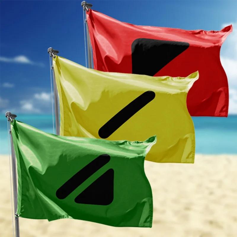 Primer plano de un mástil de playa con las tres banderas de señalización (verde, amarilla y roja) ondeando al viento, sin personas ni edificios en la imagen.