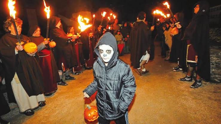 Procesión nocturna de la Güeste: vecinos cubiertos con sábanas blancas portando calabazas talladas con forma de calavera, ambiente de niebla en un pueblo cántabro