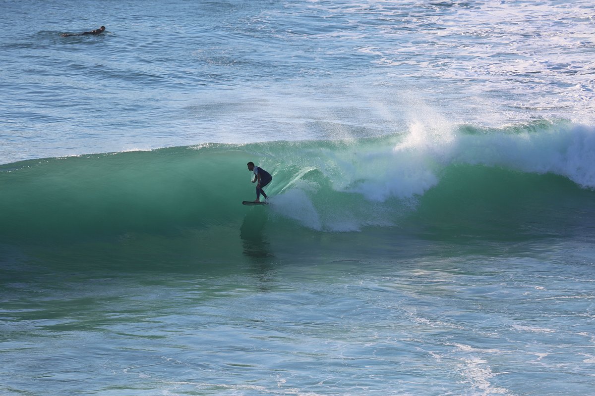 Surfista remando hacia el pico de olas en la playa de Langre, día de oleaje moderado, con el acantilado al fondo.