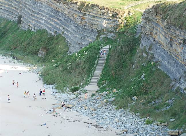 Escalera de acceso a la playa de Langre tallada en el acantilado, vista desde arriba con el mar al fondo.