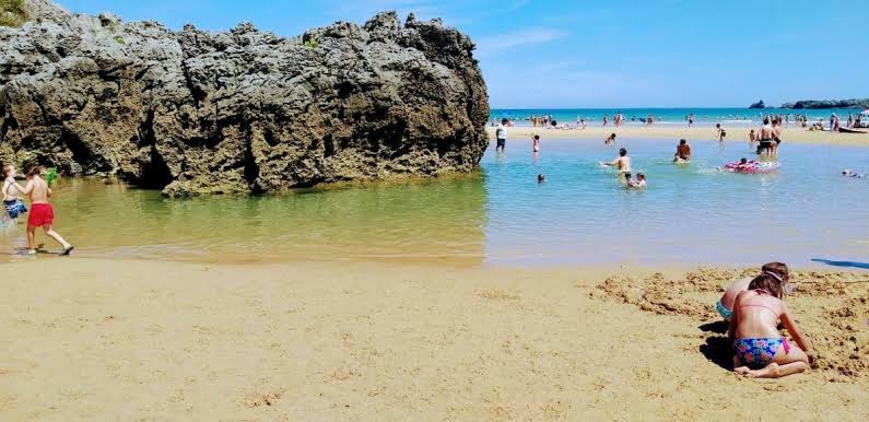 Niños jugando en la orilla con cubo y pala, marea baja en una playa de Cantabria