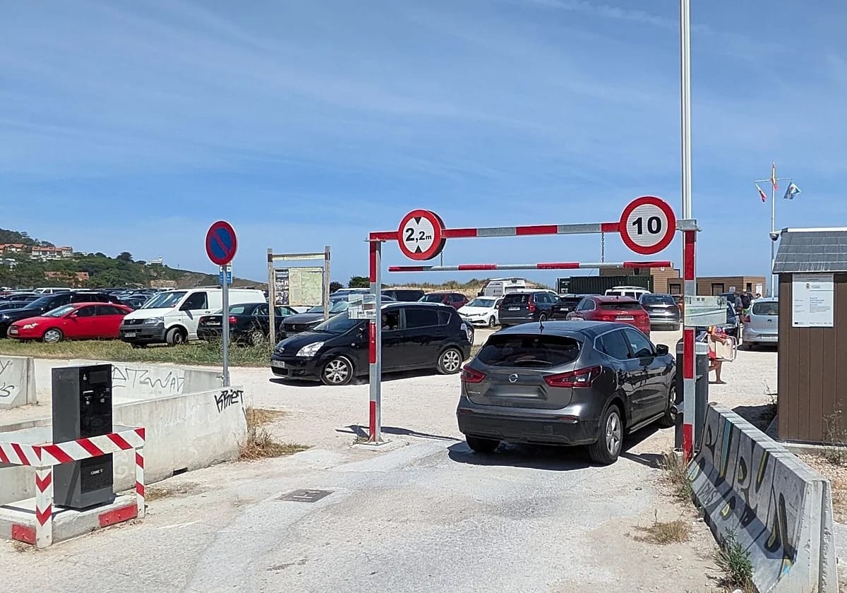 Zona de aparcamiento junto al acceso a la playa de Merón, con indicaciones hacia el arenal.
