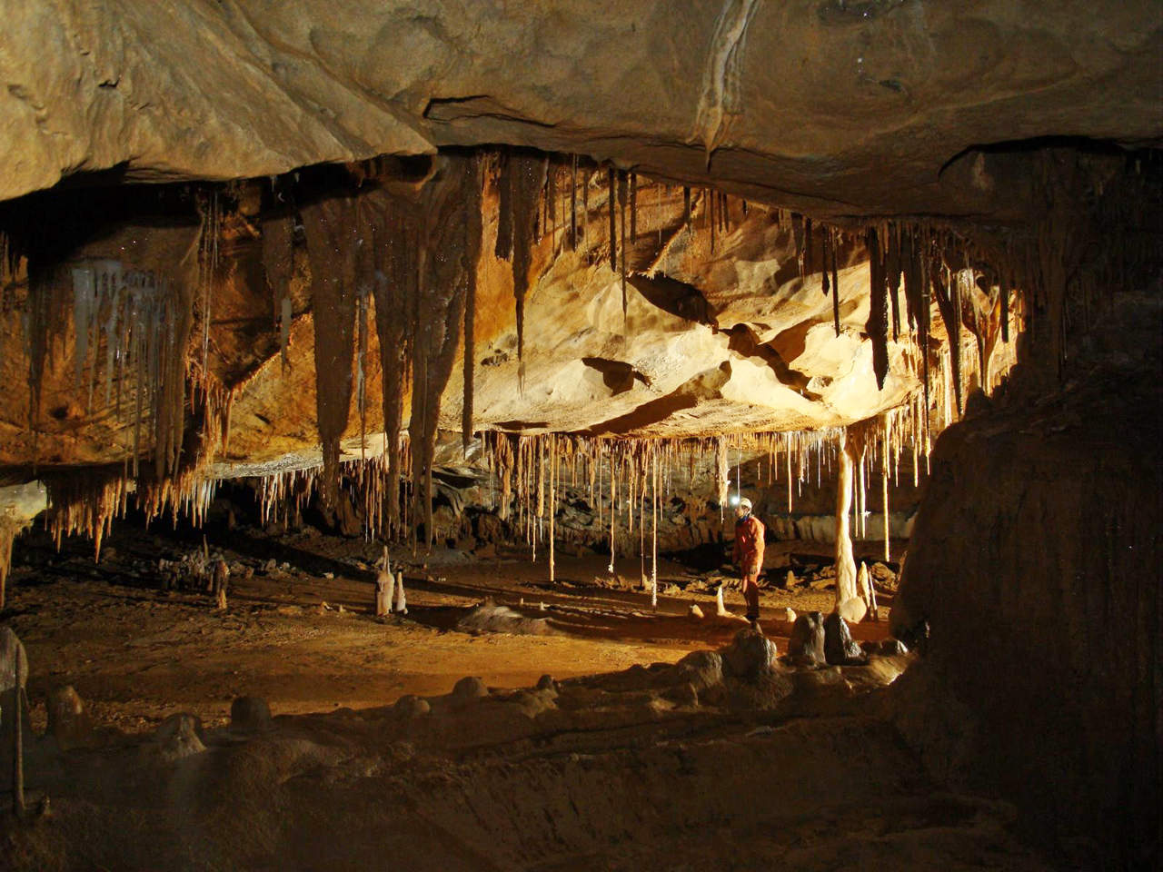 Interior de una galería subterránea iluminada solo con frontales, formaciones de roca caliza