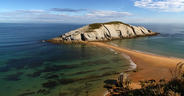Vista de la playa de Covachos y su islote con ermita, con la marea baja dejando el paso al descubierto