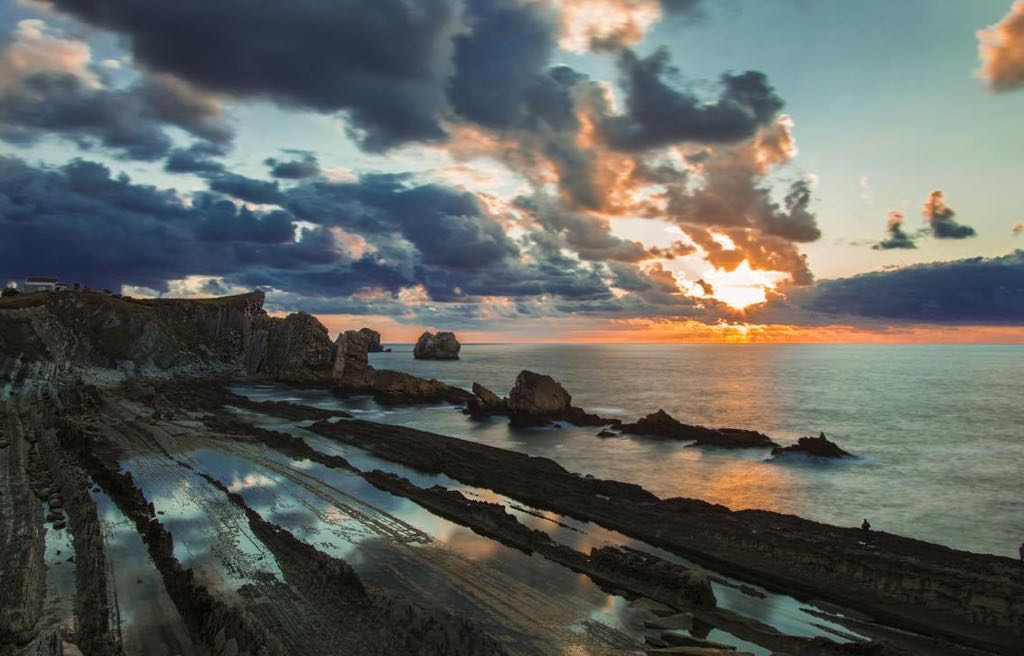 Plataforma rocosa con charcos de marea de la Playa de la Arnía y los islotes al fondo, luz de atardecer