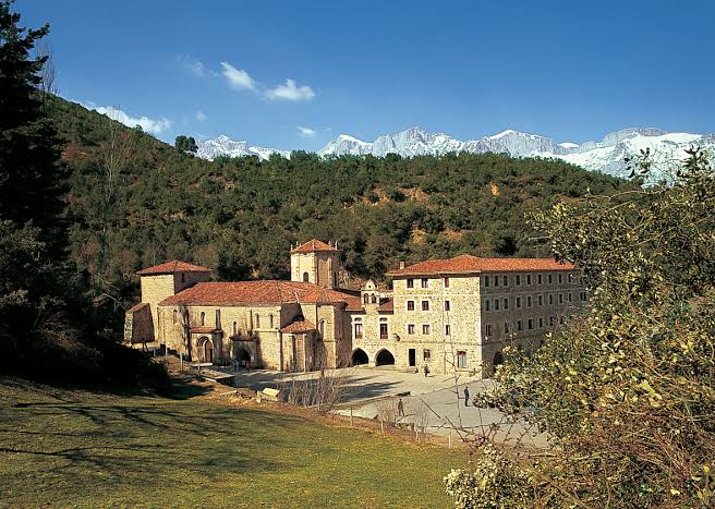 Fachada y claustro del Monasterio de Santo Toribio de Liébana, exterior de piedra con el valle detrás.