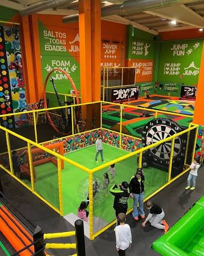 Parque de camas elásticas interior con niños saltando, colores vivos e iluminación artificial.