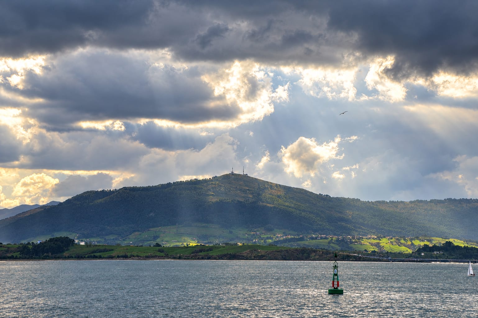 Vista de la bahía de Santander bajo un cielo nublado y lluvioso, con paraguas en primer plano.