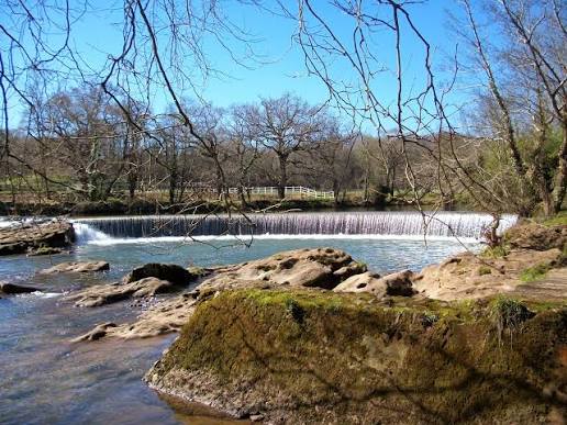 Piscina natural formada por una presa de piedra en el Parque del Camarao, Reocín, con césped y zona infantil alrededor