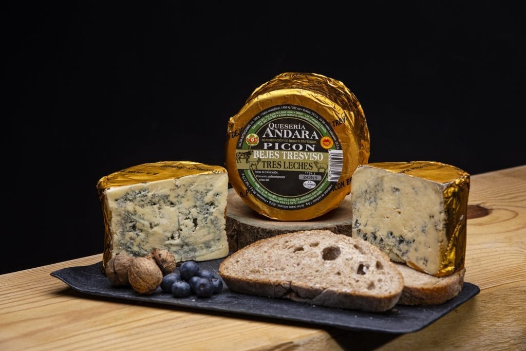 Rueda entera de queso Picón Bejes-Tresviso cortada por la mitad mostrando las vetas azules, sobre una mesa de madera