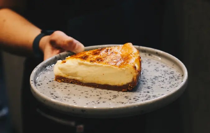 Porción rectangular de tarta pasiega de queso con mermelada de naranja amarga, mesa minimalista de Cadelo.