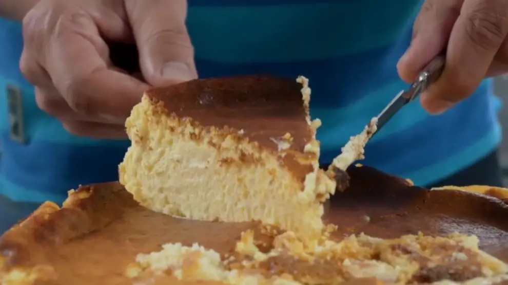 Porción de tarta tres quesos San Pelayo con textura en capas visible, vistas a los Picos de Europa detrás.