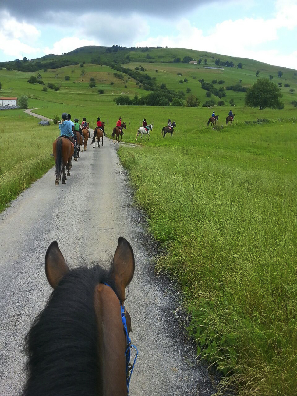 Grupo a caballo cruzando un prado verde en los Valles Pasiegos, cerca del Centro Hípico La Espina