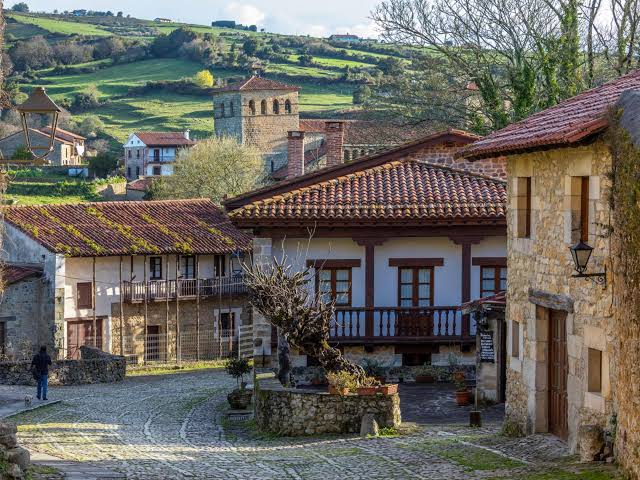 Vista panorámica de un pueblo costero de Cantabria con casas tradicionales y el mar al fondo, luz de mañana