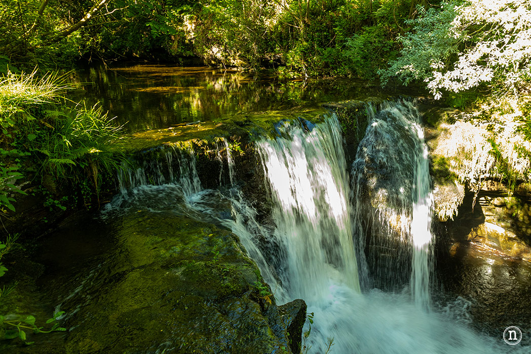 Sendero junto a un río de montaña con varios saltos de agua pequeños y un túnel de piedra excavado en la roca (ruta del Yera y el Aján, Vega de Pas).