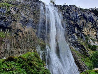 Salto de agua vertical de unos 70 metros cayendo sobre un anfiteatro rocoso en un valle verde, luz de mañana (Nacimiento del Asón, Soba).