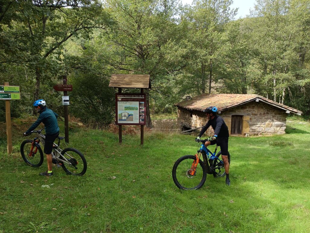 Ciclista cruzando un puente de piedra sobre el río Campiezo cerca de Güemes, luz de mañana.