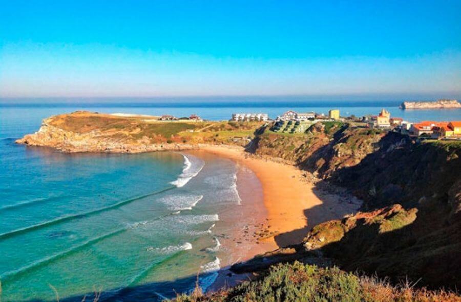 Playa de Los Locos en Suances, acantilados bajos y surfistas entrando al agua