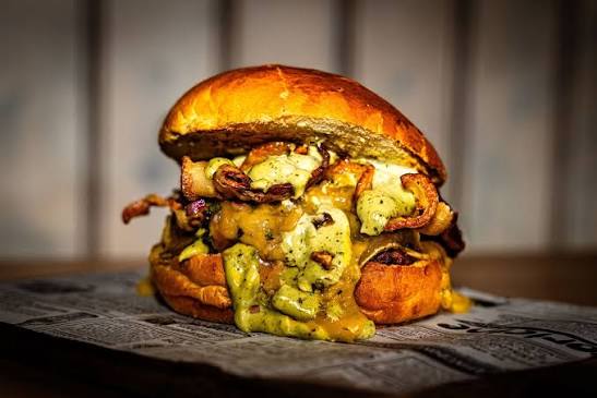 Hamburguesa smash de The Duke's servida en tabla de madera, primer plano con pan brioche dorado, interior del local en Maliaño