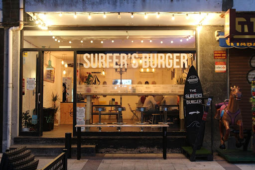 Hamburguesa de The Surfer's Burger junto a tablas de surf apoyadas en la fachada del local en Somo