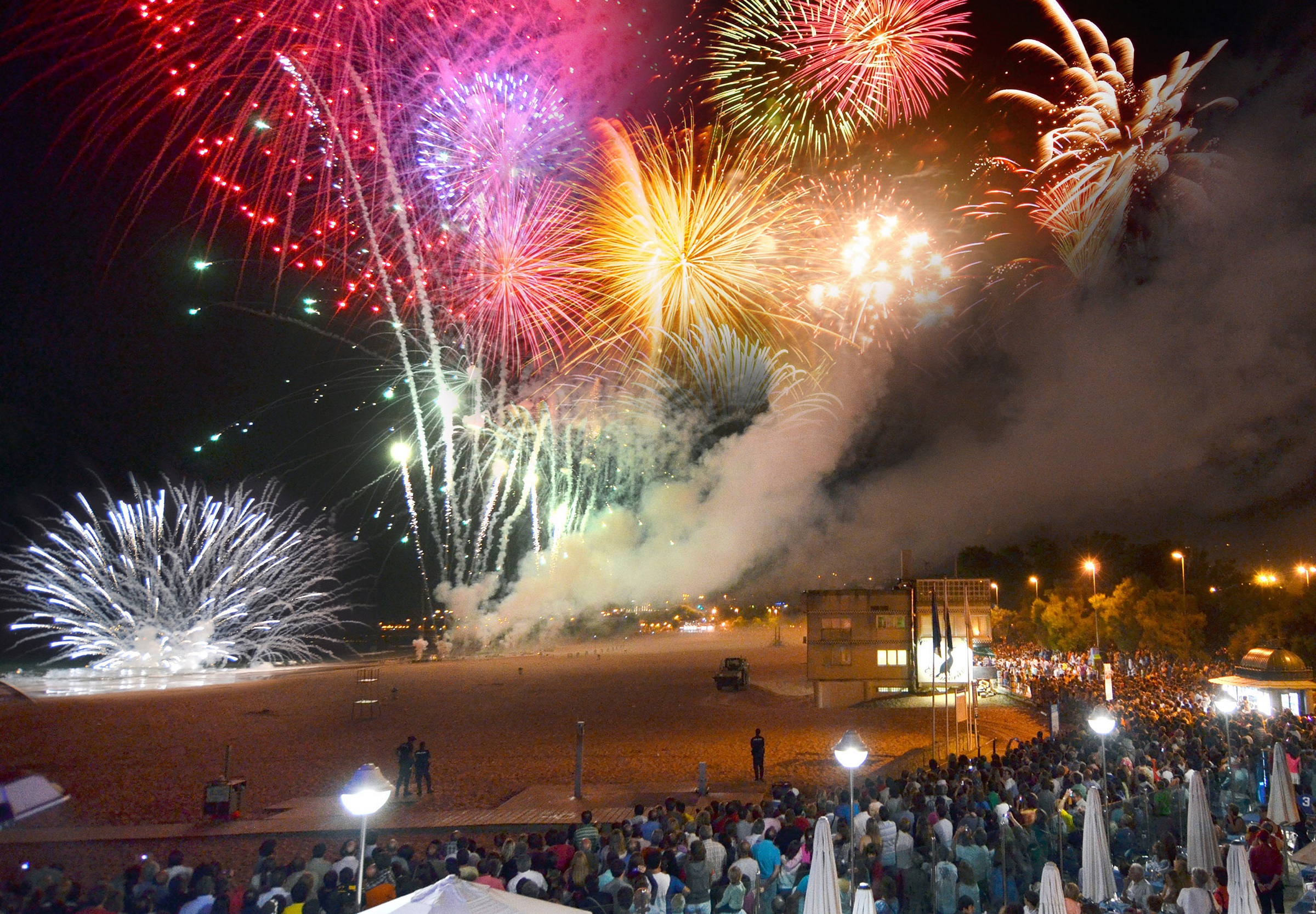 Fuegos artificiales nocturnos sobre el mar vistos desde la arena del Sardinero, con público congregado en la playa
