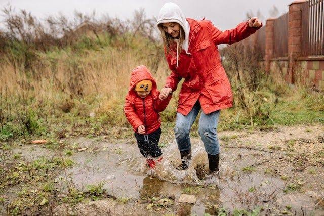 Cielo nublado y lluvia sobre el paisaje verde de Cantabria, con niños con paraguas de fondo