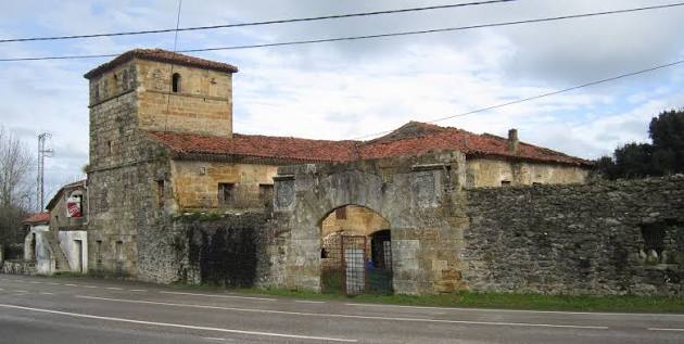Torre de piedra en ruinas parcial de una casona-torre rural, con tejado hundido y vegetación, vista desde un camino en Ajo, Bareyo