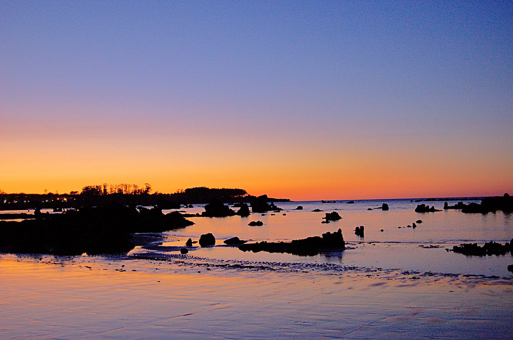 Playa de Trengandín o El Ris en Noja al atardecer, marea baja y rocas oscuras en primer plano