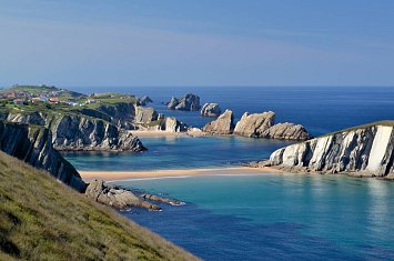 Paisaje costero de Cantabria en un día de otoño con cielo parcialmente nublado y playa poco concurrida.