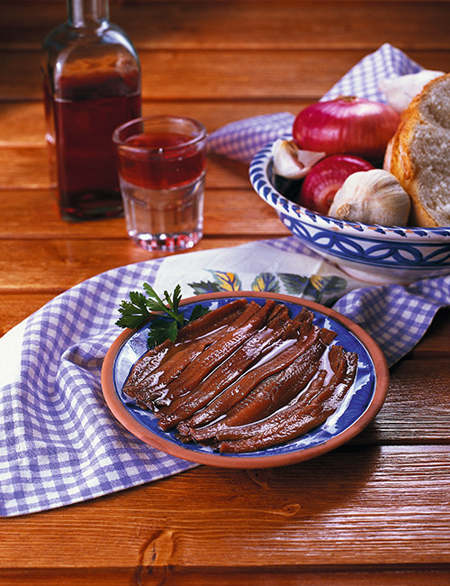 Filetes de anchoa en aceite de oliva sobre una tabla de madera, con la lata de conserva abierta al lado