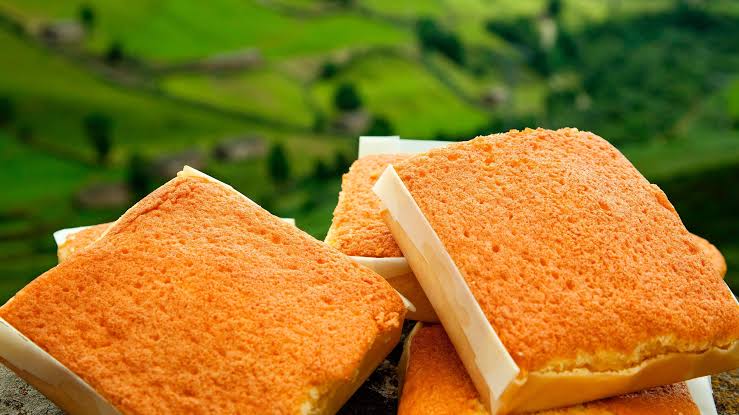 Sobaos pasiegos envueltos en su papel de horno junto a una porción de quesada pasiega en un plato, con café de fondo