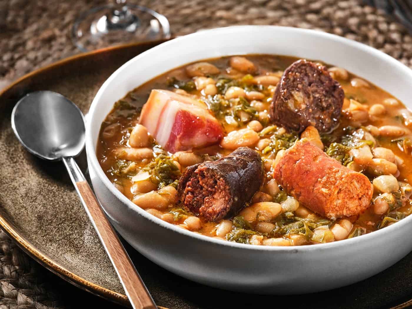 Plato de cocido montañés servido en cazuela de barro, con alubias, berza y compango, humeante