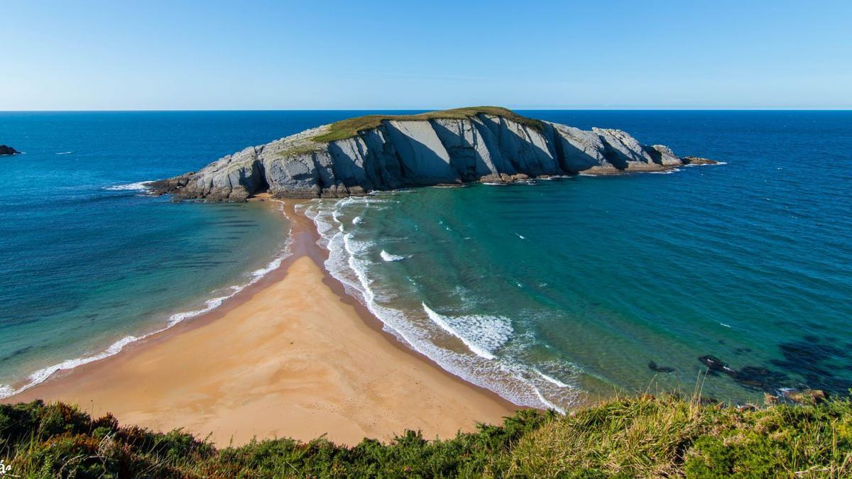 Vista general de una playa de Cantabria con la línea de marea bien visible en la arena mojada, día soleado.