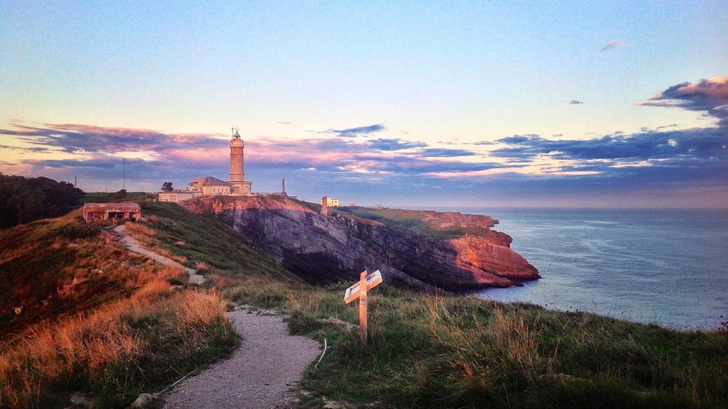 Vista panorámica de la costa de Cantabria al atardecer con un faro iluminado en el horizonte, imagen de apertura para la ruta