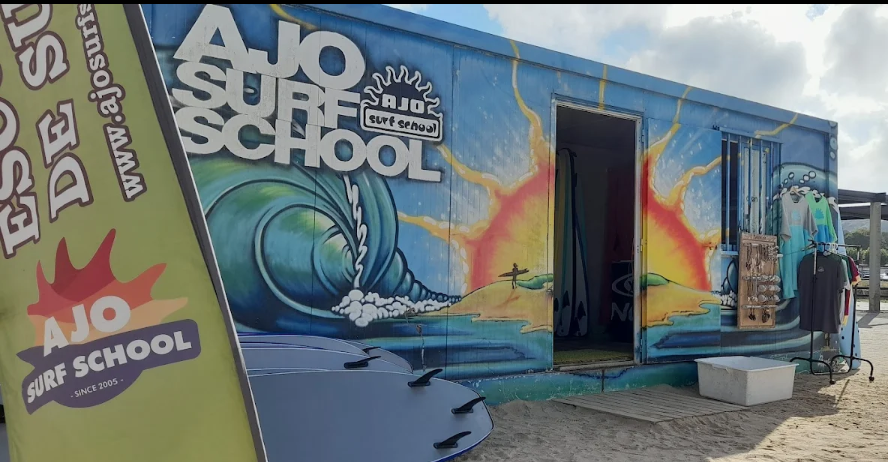 Fachada o caseta de Ajo Surf School en la playa de Cuberris, con tablas de surf visibles