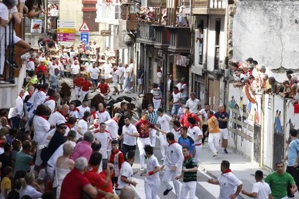 Corredores y toros cruzando el Puente Grande por la calle José Antonio de Ampuero durante uno de los encierros de mediodía.