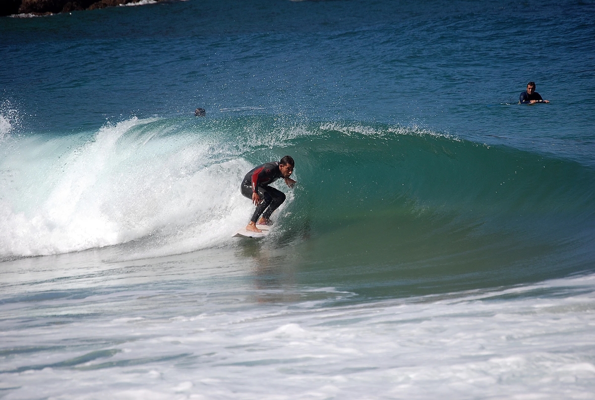 Surfista entrando al agua en una cala salvaje del norte de España con oleaje fuerte y viento.
