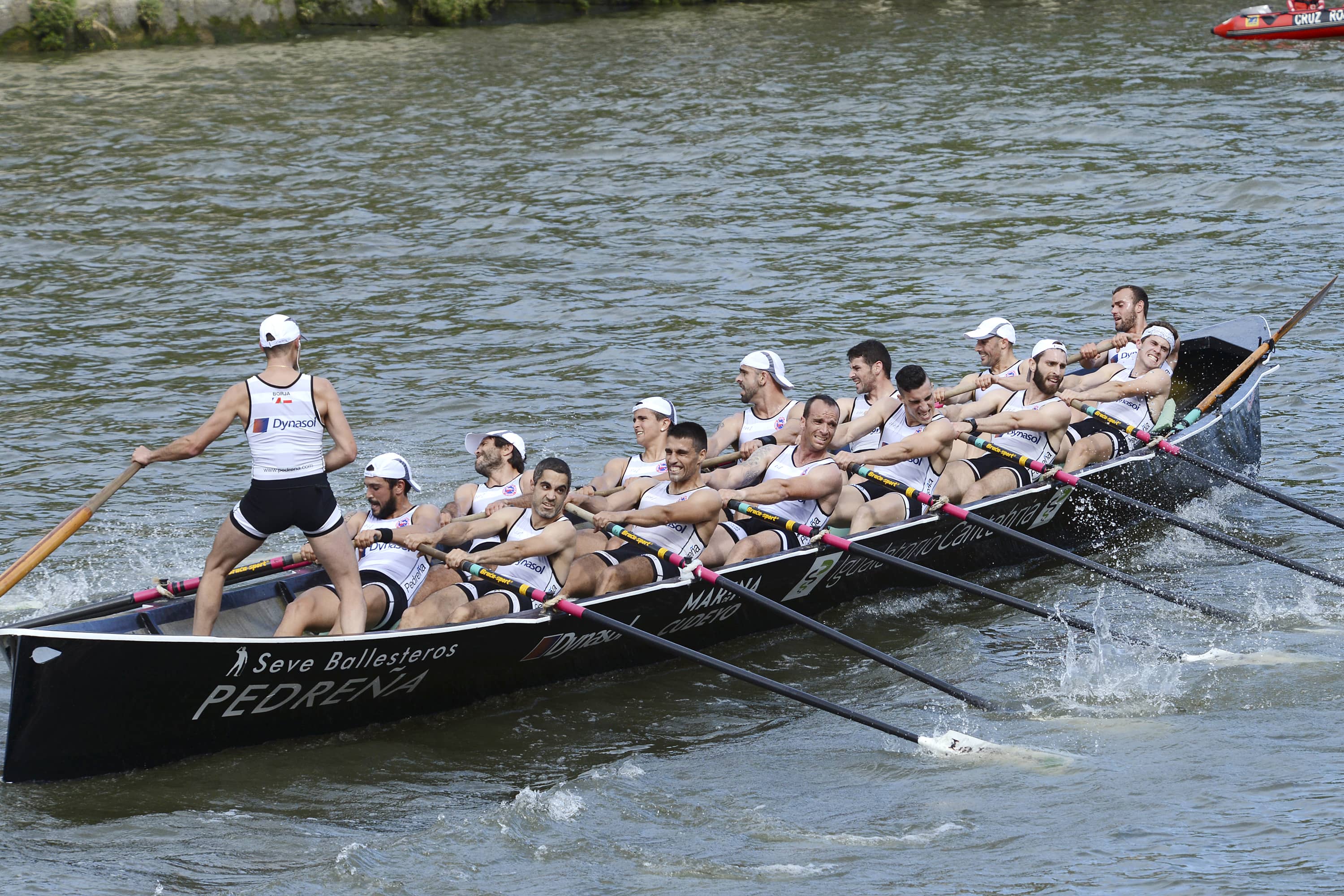 Trainera de remo en plena regata en la bahía de Santander, con remeros en pleno esfuerzo y otras embarcaciones de apoyo alrededor