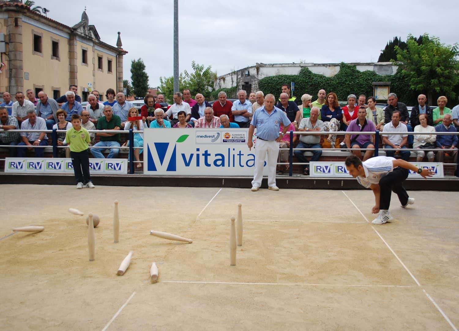 Partida de bolo palma en una bolera tradicional cántabra, bola de madera en primer plano y jugador lanzando al fondo