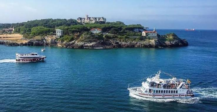Bahía de Santander con embarcaciones y el Palacete del Embarcadero al fondo, mañana despejada.
