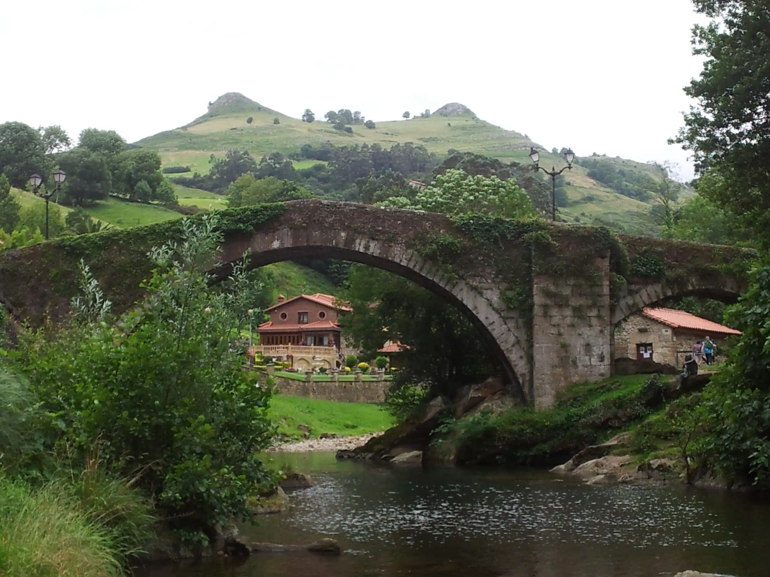 Curso del río Miera cerca de Liérganes tras un día de lluvia, caudal visiblemente más alto entre prados verdes, cielo nublado.