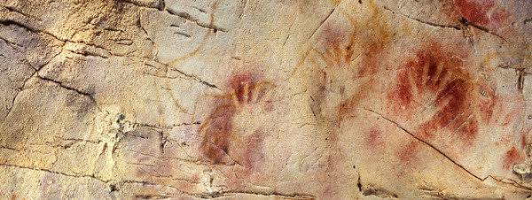 Panel de manos en negativo y siluetas de bisonte en la Cueva de El Castillo, iluminación de visita guiada.